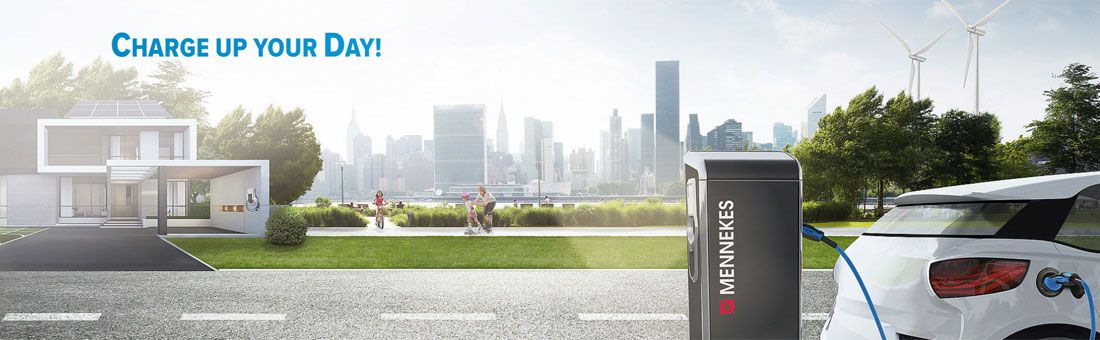 Ein weißes Elektroauto lädt an einer MENNEKES-Ladestation, im Hintergrund moderne Stadt, Windräder und ein Haus.
